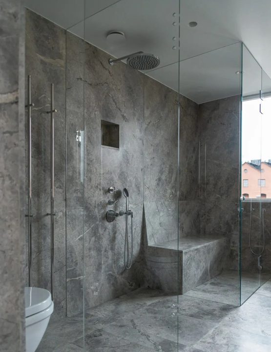 Lyxig duschhörna i marmor med glasväggar och integrerad sittbänk.