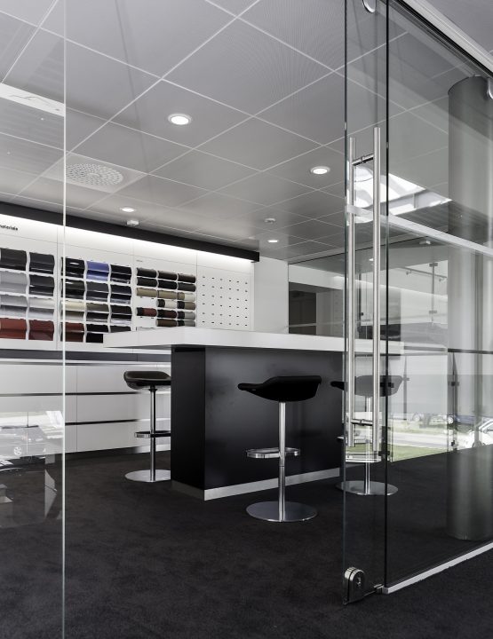 Showroom med glasväggar och kontorsplatser, Porsche-bilar utanför fönstren.