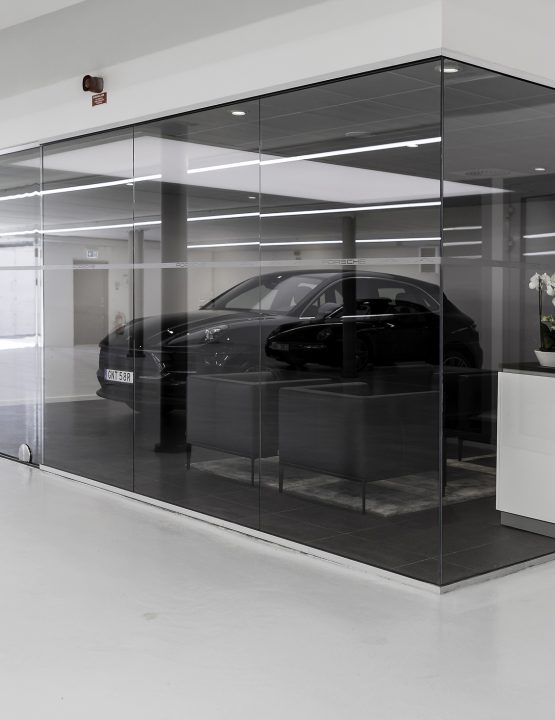 Helglasade väggar runt kundhörna i bilhall, med kaffestation och Porsche Macan i bakgrunden.