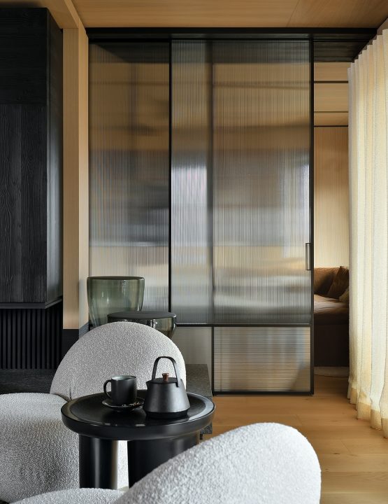 Skjutvägg i linjeglas från Albed med mörk ram som elegant avgränsar vardagsrum från annan del av hemmet i japanskinspirerad stil.