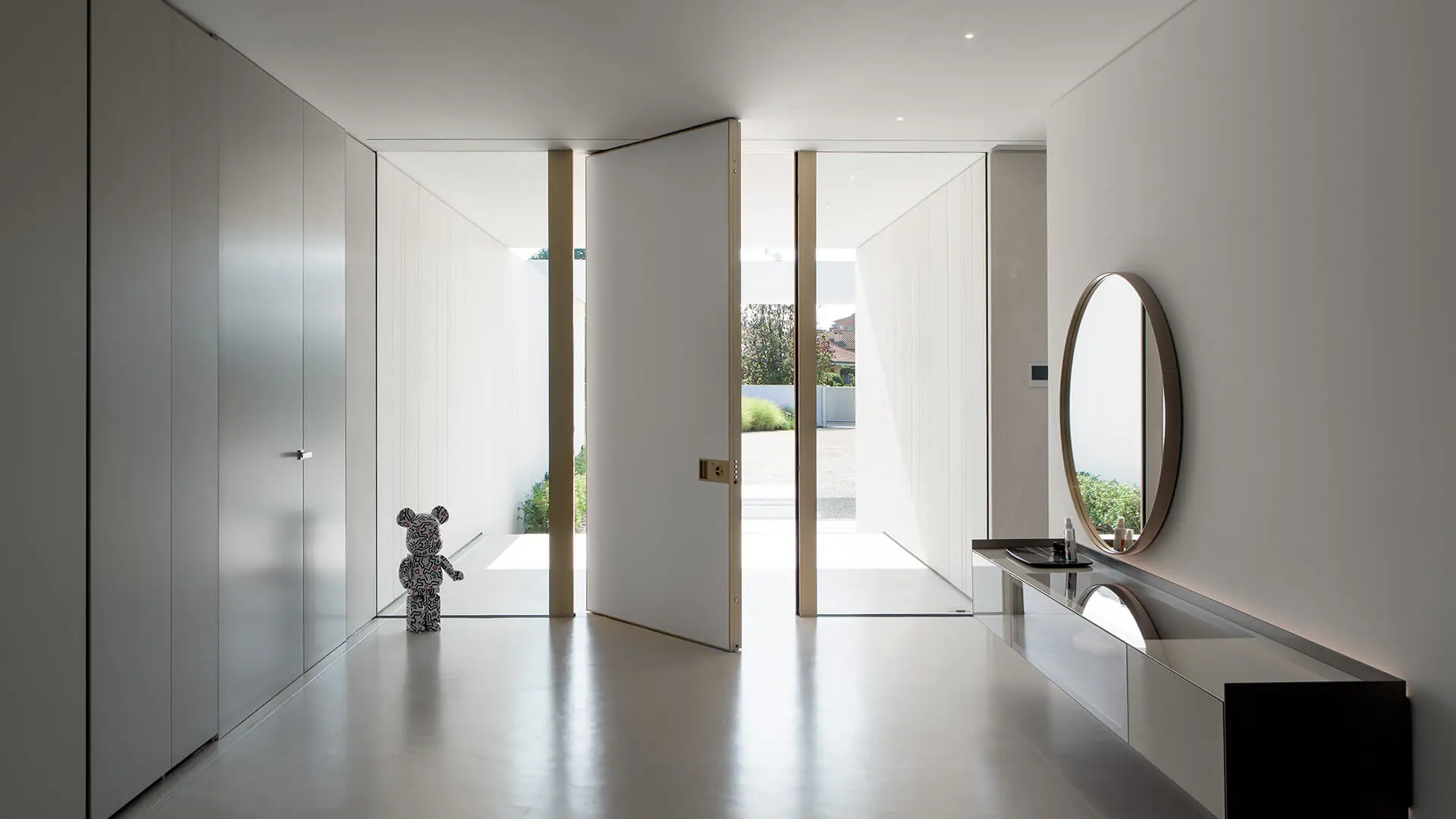 Modern pivothängd ytterdörr i minimalistisk entré med glaspartier